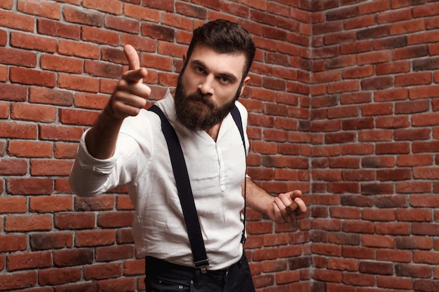 Brutal rage young handsome man smoking cigar on brick wall.