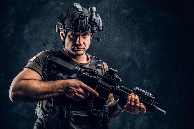 Brutal soldier of the Russian Federation wearing body armor and helmet with a night vision posing with an assault rifle. Studio photo against a dark textured wall