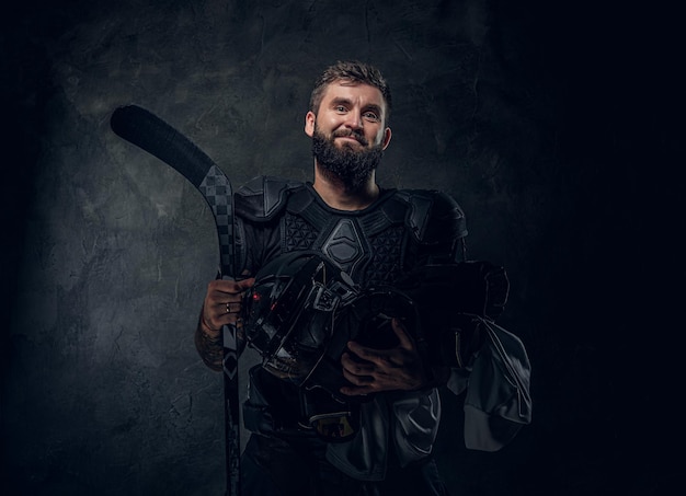 Brutal tattooed hockey player is posing for photographer at dark photo studio.