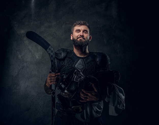 Brutal tattooed hockey player is posing for photographer at dark photo studio.