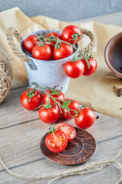 Bucket of tomatoes and half cut tomato on wooden table.