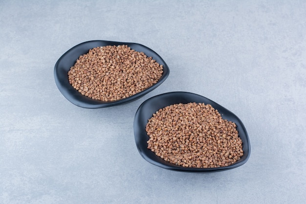 Buckwheat groats piled in two bowls on marble background.