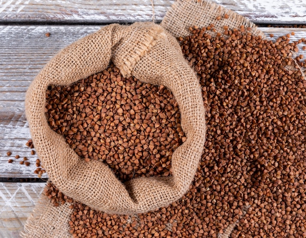 Buckwheats in a sack on a sack cloth and light wooden . flat lay.