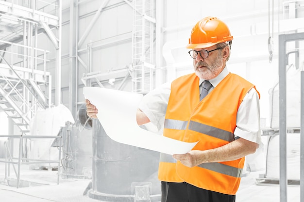 Free photo the builder in a construction vest and orange helmet standing on white studio wall