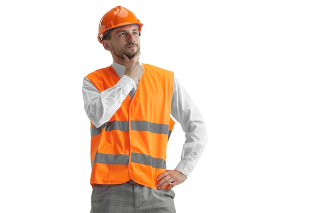 Free photo the builder in a construction vest and orange helmet standing on white wall. safety specialist, engineer, industry, architecture, manager, occupation, businessman, job concept