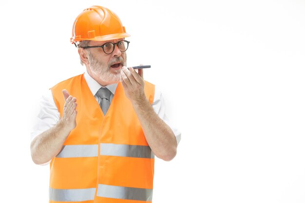 builder in a construction vest and an orange helmet talking on a mobile phone about something.