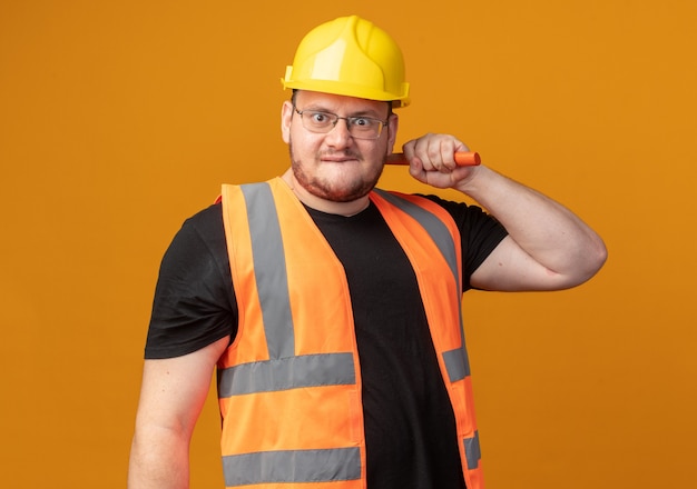 Free photo builder man in construction vest and safety helmet holding hammer looking at camera with angry face