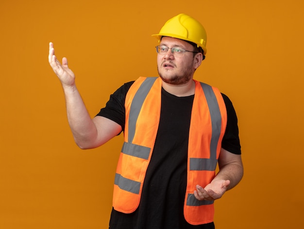 Free photo builder man in construction vest and safety helmet looking aside confused with arms raised