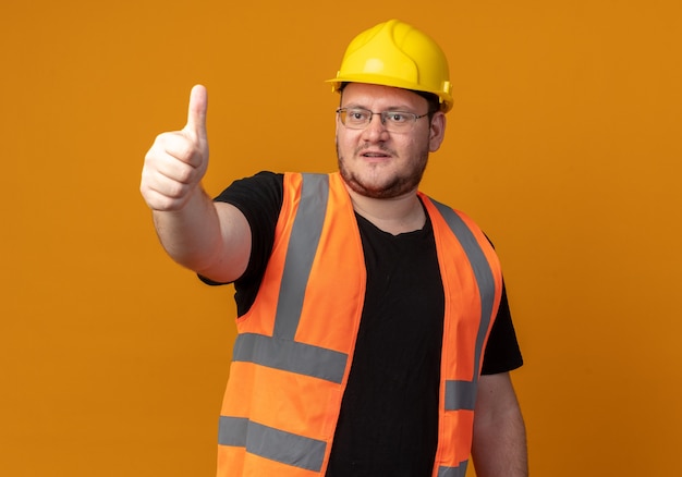 Free photo builder man in construction vest and safety helmet looking aside smiling confident showing thumbs up standing over orange background