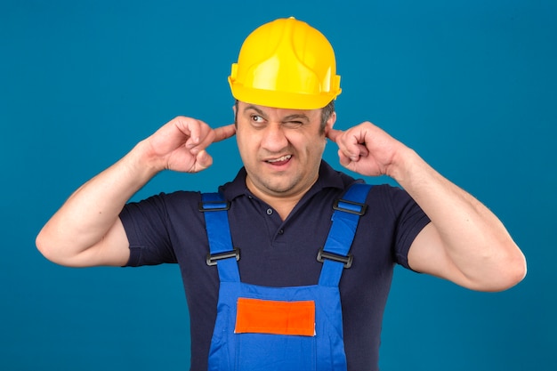 Free photo builder man wearing construction uniform and safety helmet closing ears because of noise over isolated blue wall