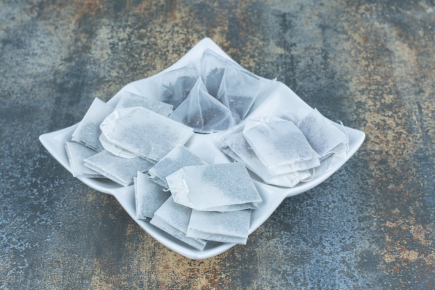 Bunch of black teabags on white plate.