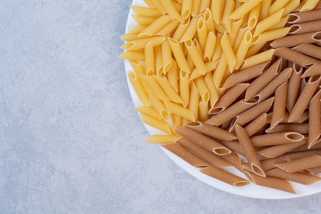 Free photo bunch of brown and yellow penne pasta on white plate