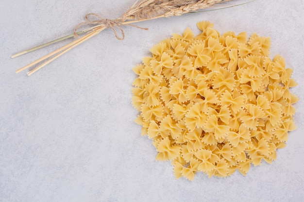 Free photo bunch of farfalle pasta on white table with wheat.