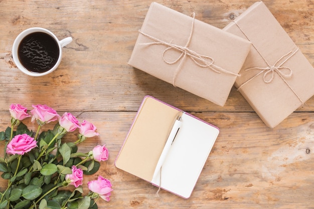 Bunch of flowers with gift boxes; diary and black tea on wooden backdrop