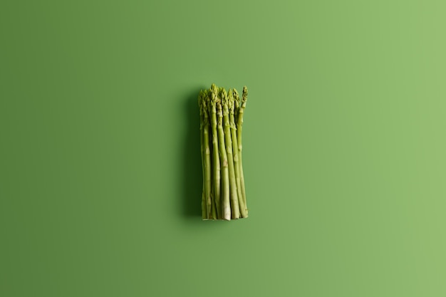 Free photo bunch of fresh asparagus on vivid green background. ingredient for preparing delicious vegetarian salad. food concept. fresh spring vegetables. edible sprouts of asparagus rich in vitamins, folic acid