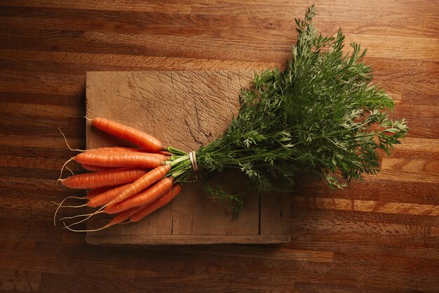 A bunch of fresh carrots on a weathered old cutting board with deep cuts on a beautiful wooden brown table, top view