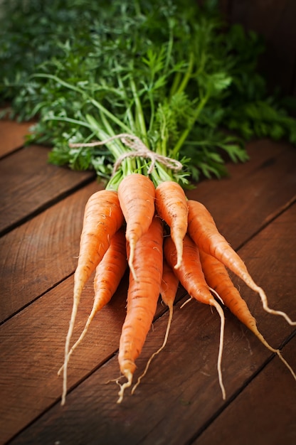 Free photo bunch of fresh carrots with green leaves over wooden table