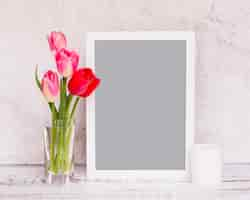 Free photo bunch of fresh flowers on stems in vase near frame and candle