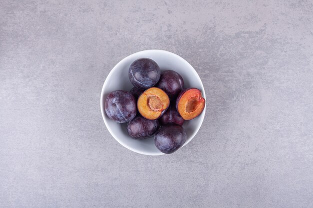 Bunch of fresh purple plums placed in white bowl. 