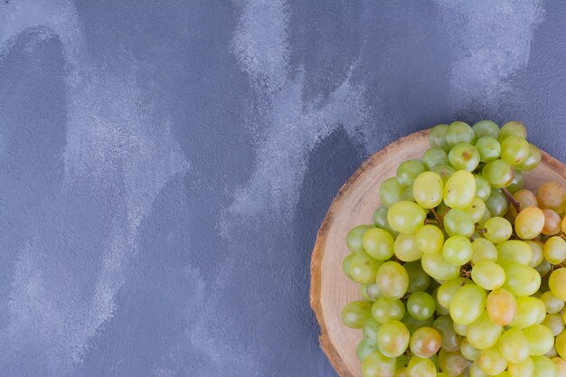 A bunch of green grapes on wooden platter.