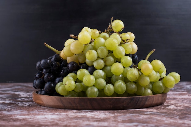 A bunch of green and red grapes in a wooden platter on black