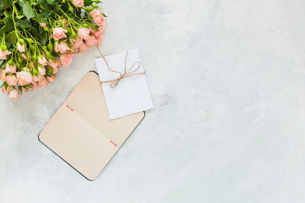 Bunch of pink roses; envelope and notebook on concrete background