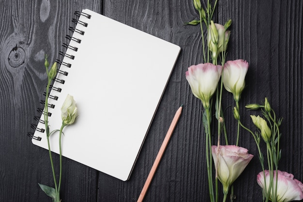 Free photo bunch of purple eustoma flowers with pencil and blank spiral notepad on wooden desk