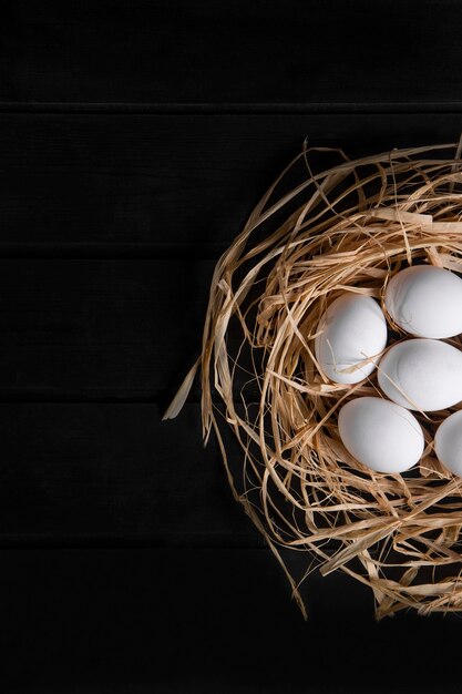 Bunch of raw fresh eggs in bird's nest on black surface. High quality photo