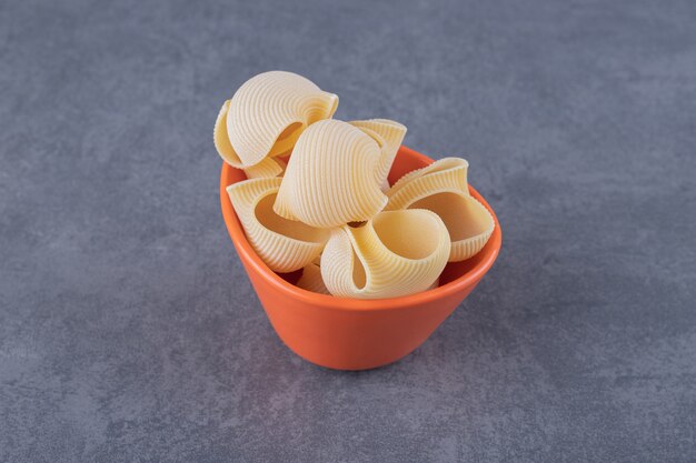 Bunch of raw shell pasta in orange bowl.