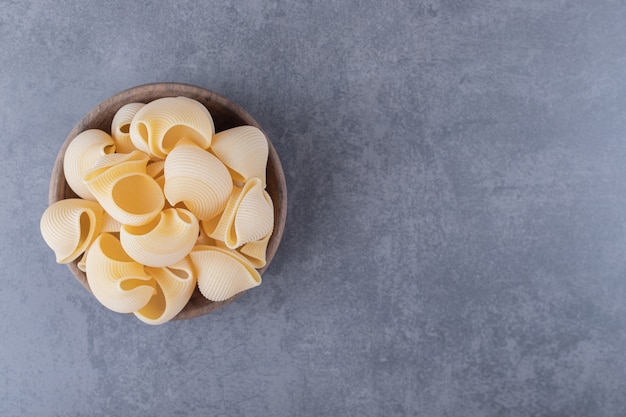 Free photo bunch of raw shell pasta in wooden bowl.