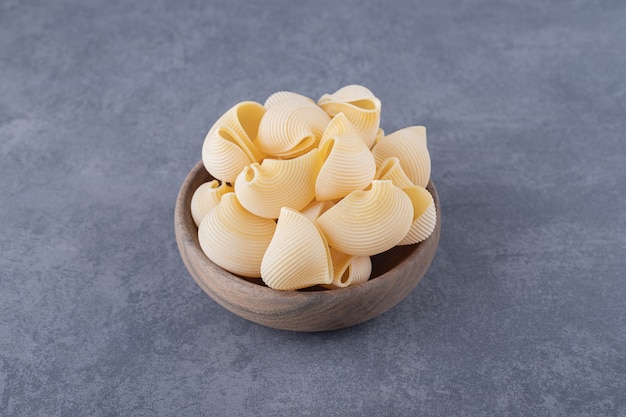 Bunch of raw shell pasta in wooden bowl.