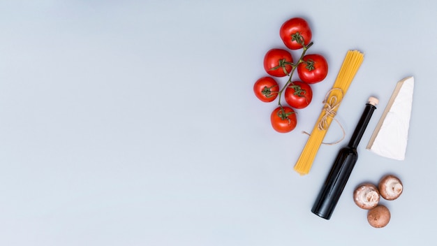 Free photo bunch of raw spaghetti pasta; tomato; mushroom; cheese and oil bottle for making tasty pasta