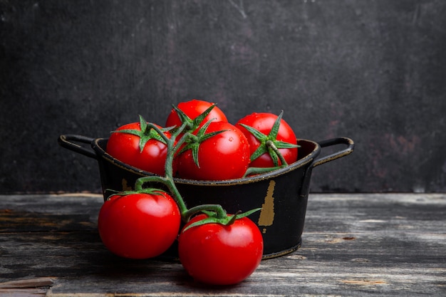 Free photo a bunch of tomatoes in a pot on a old wooden and black background. side view.