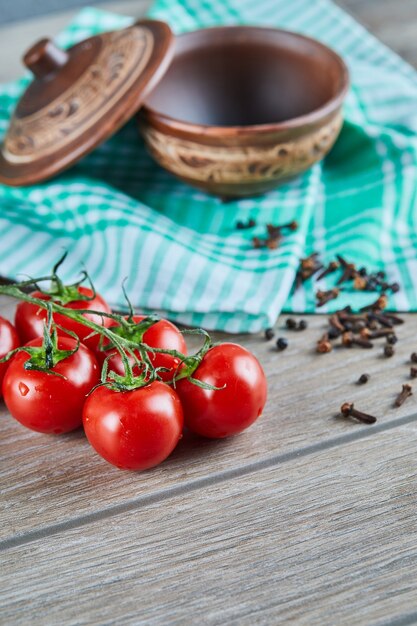 Bunch of tomatoes with branch and empty bowl with cloves on wooden table