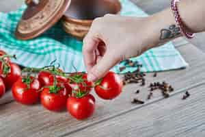 Free photo bunch of tomatoes with branch and woman holding a tomato on wooden table