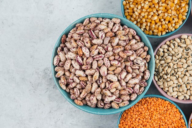 Bunch of various uncooked beans, corns and red lentils on marble surface.