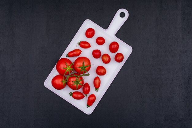 Bunches of tomato and red cherry tomato on white cutting board over black stone surface