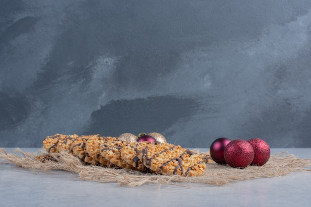 Bundle of cookies and christmas baubles on a piece of cloth on marble surface