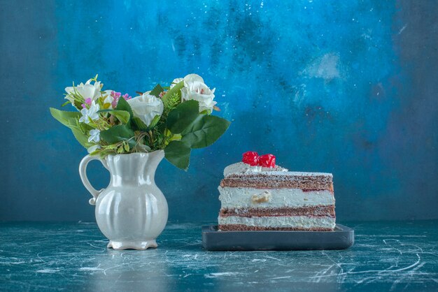 Bundle of flowers next to a small slice of cake on blue background. High quality photo