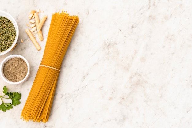 Bundle of uncooked spaghetti pasta and ingredient on marble textured background