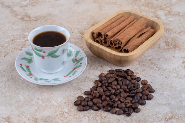 Bundles of cinnamon sticks and coffee beans next to a cup of coffee 