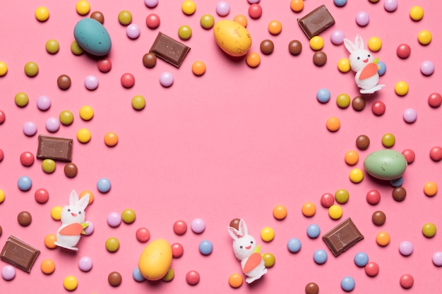 Bunny figurine; gem candies; chocolate easter eggs with space in the center on pink background