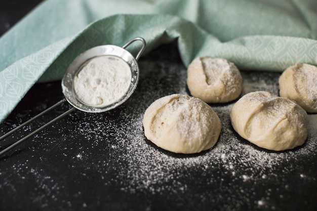 Buns bread dough ready to bake with flour on black backdrop