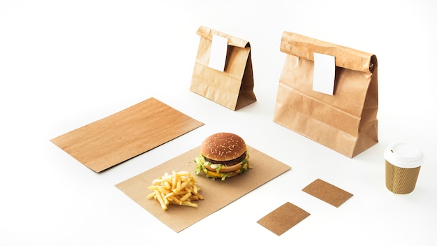 Free photo burger and french fries on paper with disposable drink and paper package on white backdrop