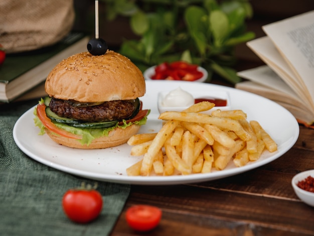 A burger served with french fries and sauces in a plate on a rustic table.