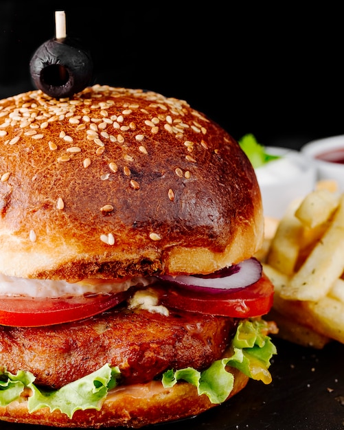 Burger with meat and vegetables in bread bun.