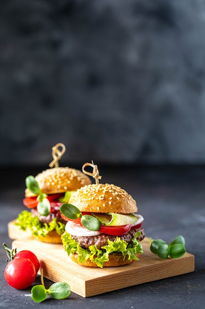 Burgers with meat cutlet, fresh lettuce, tomatoes, onions on a dark stone. copy space