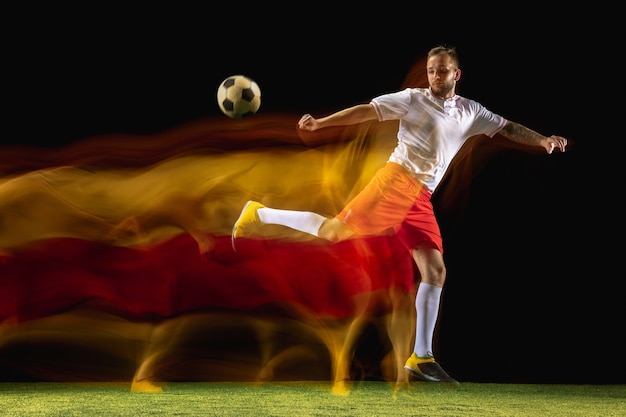 Free photo burning. young caucasian male football or soccer player in sportwear and boots kicking ball for the goal in mixed light on dark wall. concept of healthy lifestyle, professional sport, hobby.