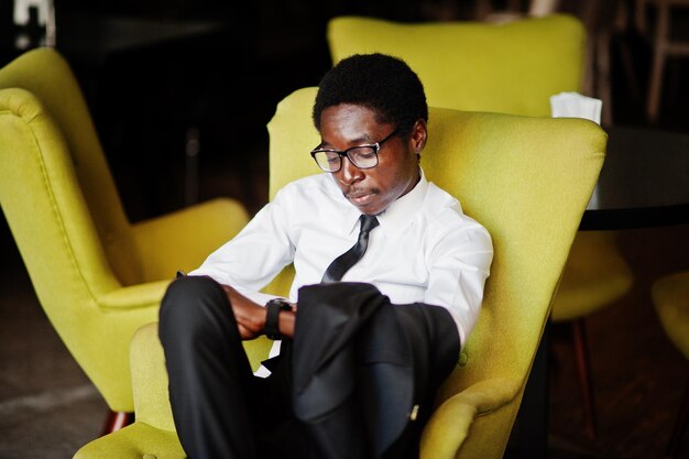 Business african american man wear on white shirt tie and glasses at office sitting on chair and looking at watches