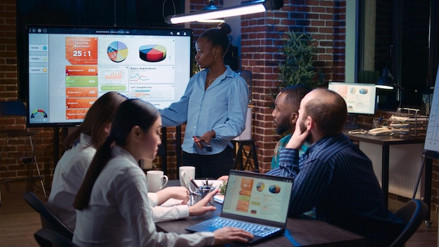 Business analytics meeting, african american project manager showing corporate presentation, team discussing statistics, planning sales strategy. Coworkers watching diagrams at digital board